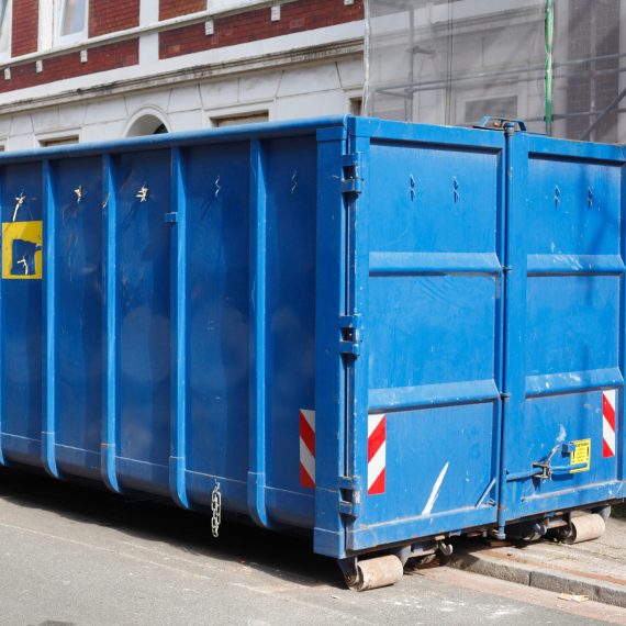 Blaue Absetzmulde für Bauschutt, auf der Straße vor einem Haus mit Baustelle stehend